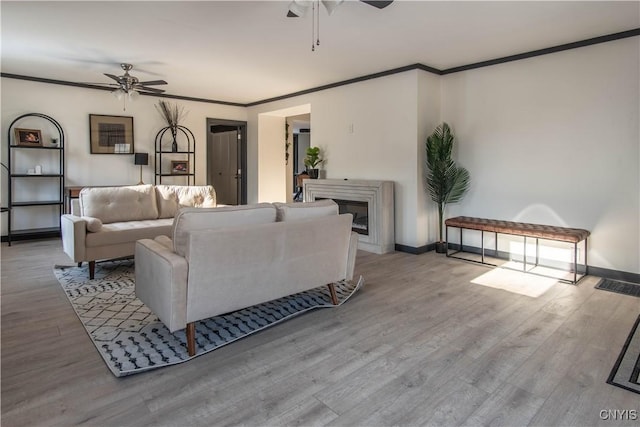 living room with a glass covered fireplace, ornamental molding, a ceiling fan, and wood finished floors