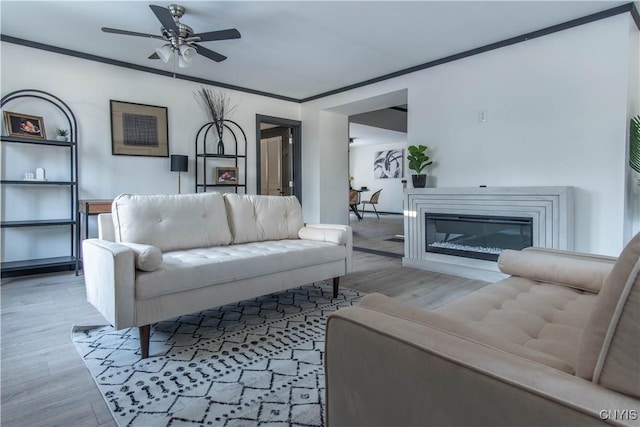 living area with a glass covered fireplace, ornamental molding, and wood finished floors