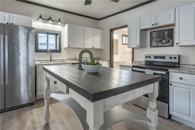 kitchen featuring a sink, light wood-style floors, appliances with stainless steel finishes, white cabinets, and crown molding