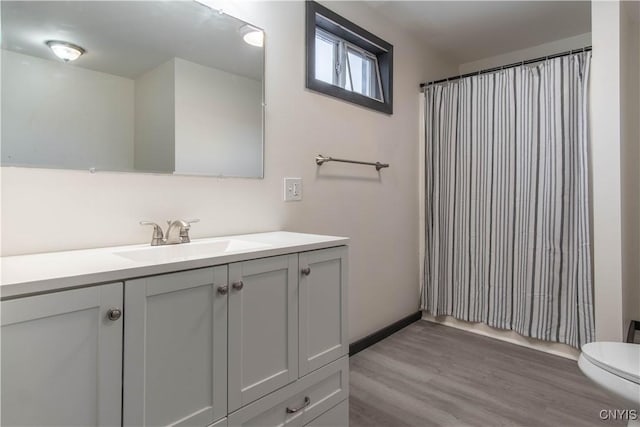 bathroom featuring toilet, wood finished floors, a shower with shower curtain, baseboards, and vanity