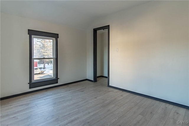 spare room with baseboards, lofted ceiling, and light wood-style flooring