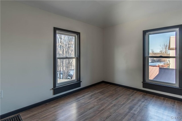 unfurnished room featuring dark wood finished floors, visible vents, and baseboards