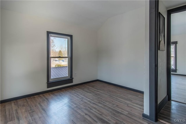 spare room featuring dark wood-style floors, baseboards, and vaulted ceiling