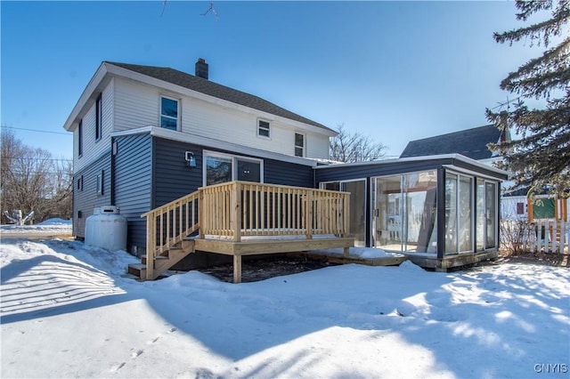 snow covered house featuring a deck, a chimney, and a sunroom