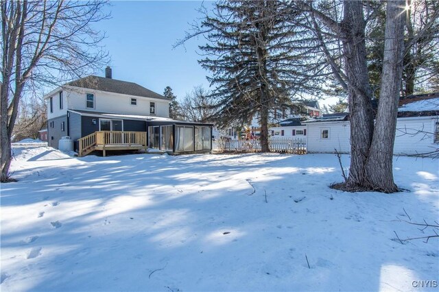 snow covered house with a wooden deck and a chimney