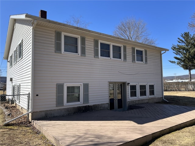 back of house featuring french doors, a chimney, a deck, and fence