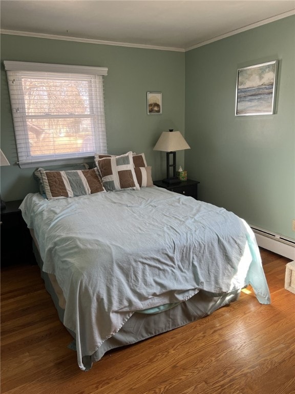 bedroom with crown molding, a baseboard heating unit, and wood finished floors