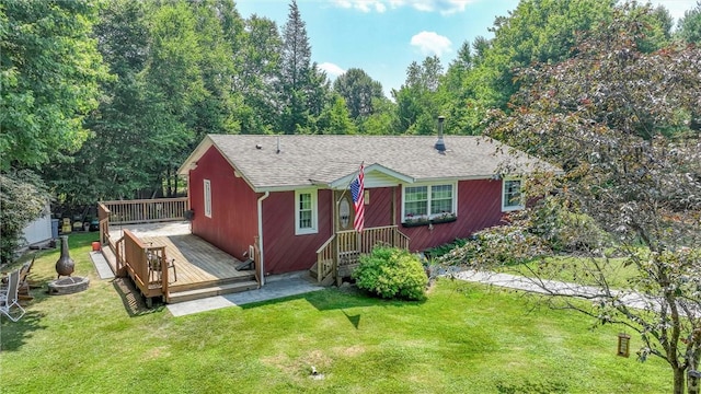 view of front of property with a deck, a front yard, roof with shingles, and an outdoor fire pit