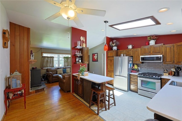 kitchen featuring stainless steel appliances, vaulted ceiling, brown cabinetry, and light countertops