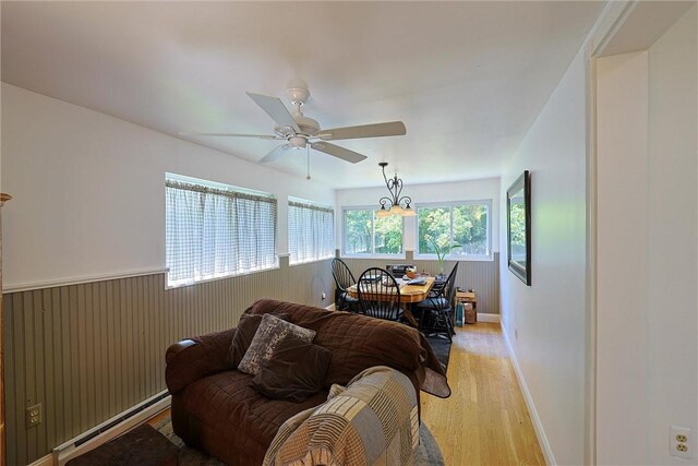 living area featuring a ceiling fan, a wainscoted wall, a baseboard radiator, light wood-style floors, and wood walls