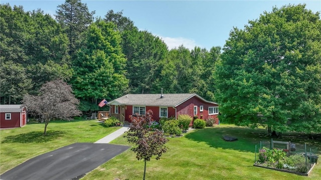 ranch-style house featuring a shed, a front yard, an outdoor structure, a garden, and driveway