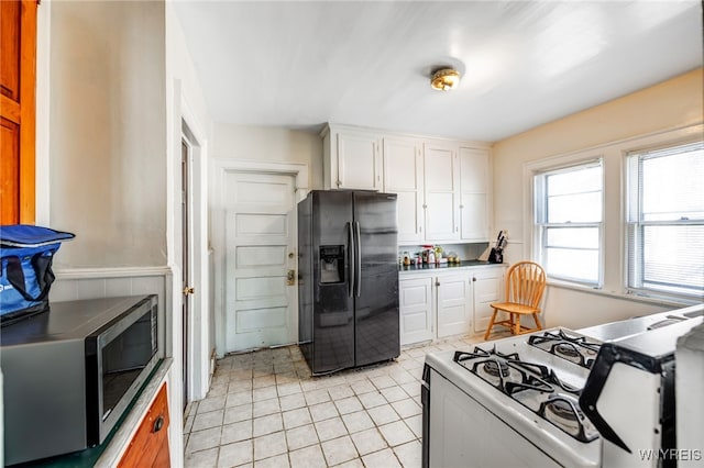 kitchen with stainless steel microwave, white gas range, light tile patterned floors, black fridge, and white cabinetry