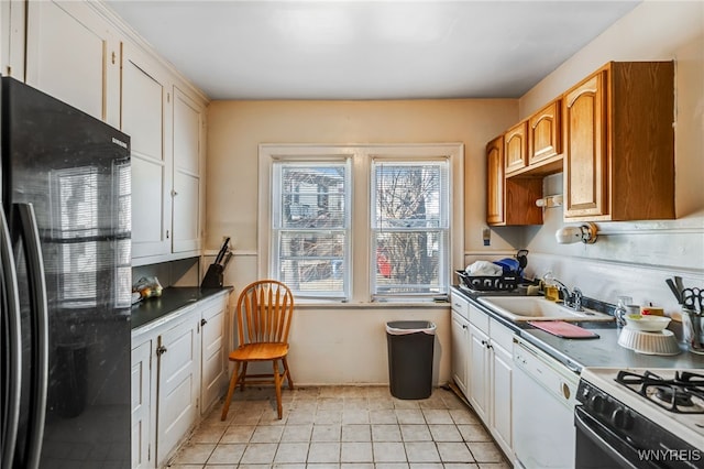 kitchen with light tile patterned floors, freestanding refrigerator, a sink, dishwasher, and dark countertops