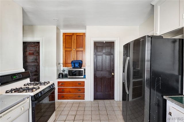 kitchen featuring fridge with ice dispenser, stainless steel microwave, range with gas stovetop, light tile patterned flooring, and white cabinets