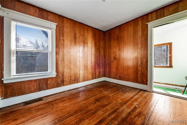 spare room with wooden walls, visible vents, baseboards, and hardwood / wood-style flooring