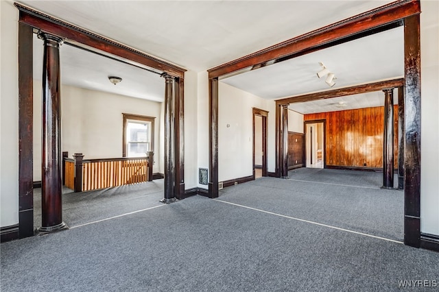 empty room featuring beam ceiling, wooden walls, carpet, and ornate columns