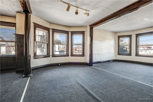 unfurnished room featuring ornate columns, track lighting, baseboards, and carpet