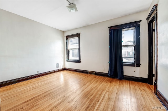 unfurnished room with light wood finished floors, visible vents, and baseboards