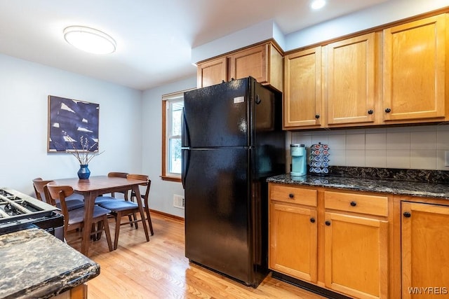 kitchen with dark stone countertops, tasteful backsplash, freestanding refrigerator, gas stove, and light wood-style floors