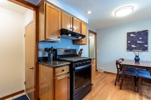 kitchen featuring visible vents, stainless steel gas stove, under cabinet range hood, dark stone countertops, and light wood finished floors