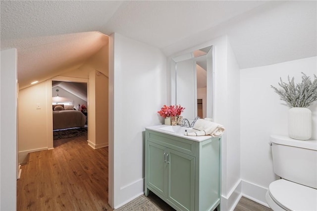 bathroom featuring toilet, vanity, vaulted ceiling, wood finished floors, and a textured ceiling