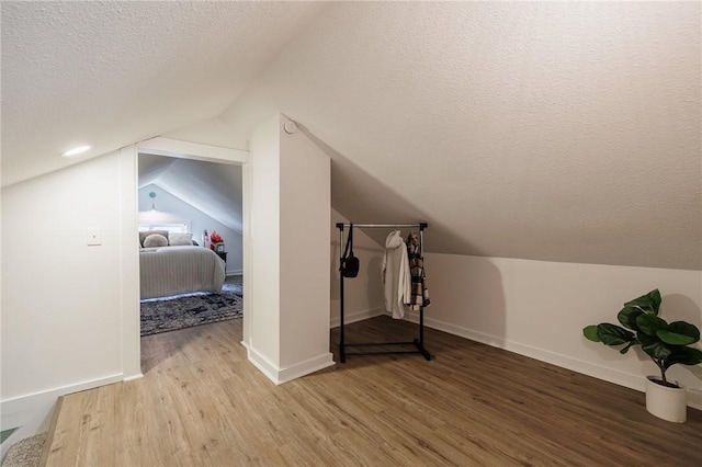 additional living space featuring vaulted ceiling, wood finished floors, baseboards, and a textured ceiling