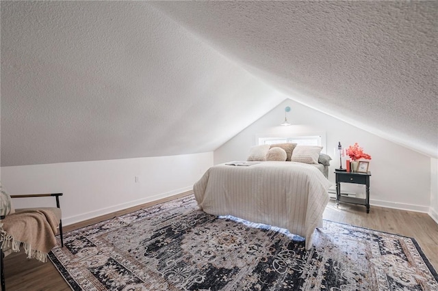 bedroom featuring baseboards, lofted ceiling, a textured ceiling, and wood finished floors