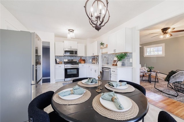 dining space with light wood finished floors, ceiling fan with notable chandelier, and ornamental molding