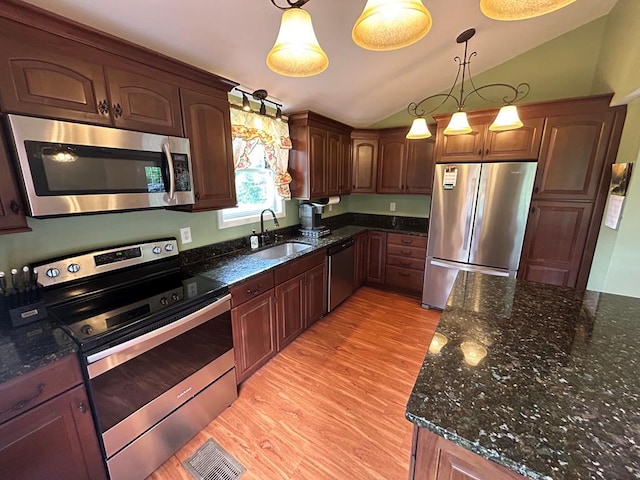 kitchen featuring light wood-type flooring, a sink, dark stone countertops, appliances with stainless steel finishes, and lofted ceiling