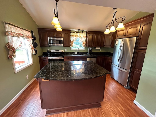 kitchen featuring light wood-type flooring, a sink, a kitchen island, appliances with stainless steel finishes, and vaulted ceiling