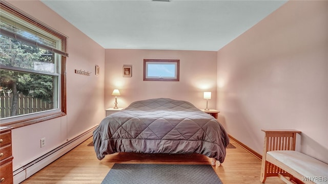 bedroom featuring a baseboard heating unit, baseboards, and light wood finished floors