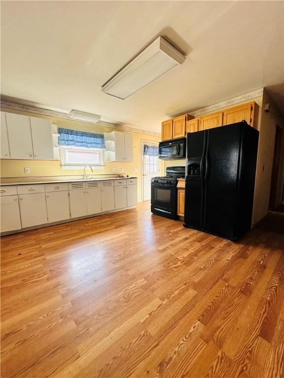 kitchen with light wood-style flooring, black appliances, light countertops, and a sink