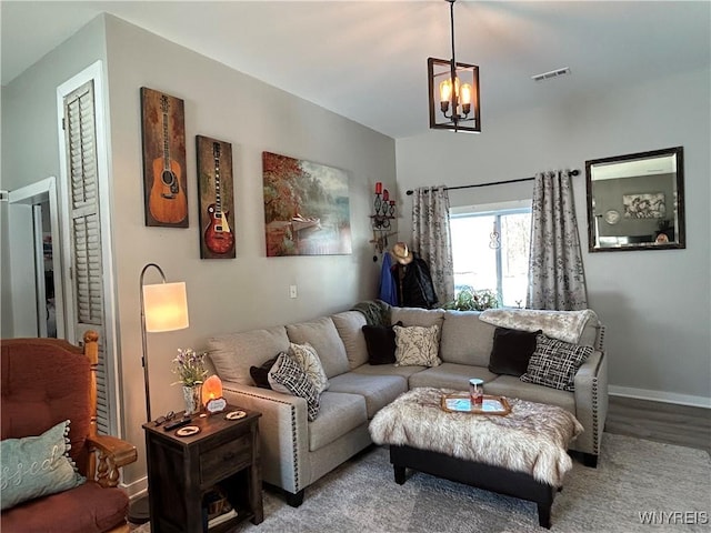 living area featuring a notable chandelier, visible vents, baseboards, and wood finished floors