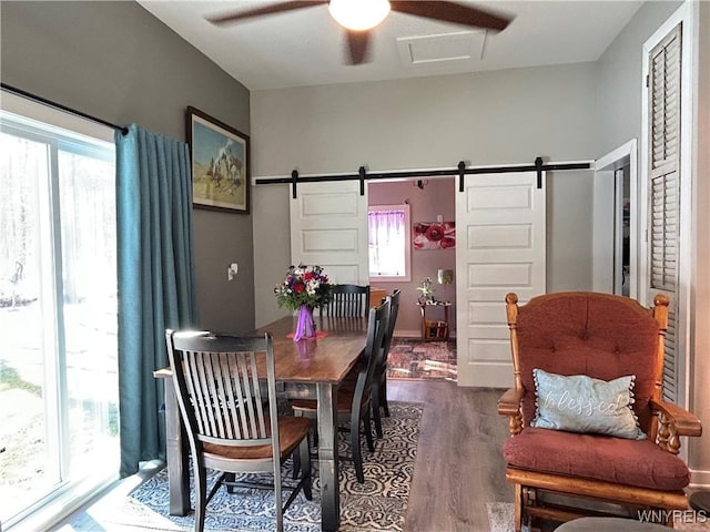 dining area with a ceiling fan, a barn door, and wood finished floors