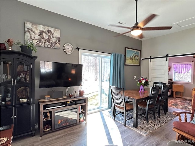 dining space with a healthy amount of sunlight, a ceiling fan, a barn door, and wood finished floors