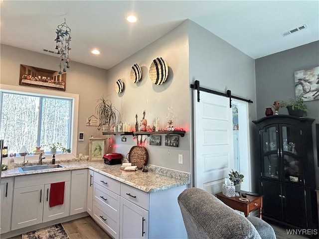 kitchen featuring visible vents, light wood finished floors, a sink, white cabinets, and a barn door