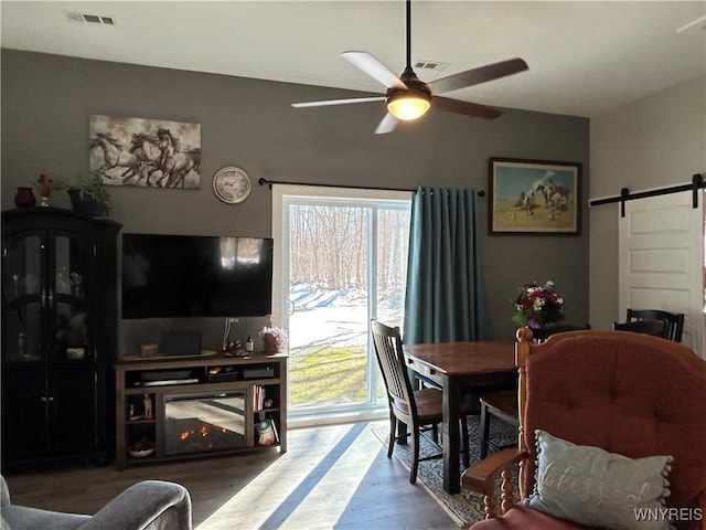 dining room with visible vents, a ceiling fan, a barn door, and wood finished floors