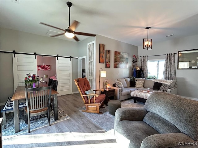 living area featuring ceiling fan with notable chandelier, a barn door, and wood finished floors