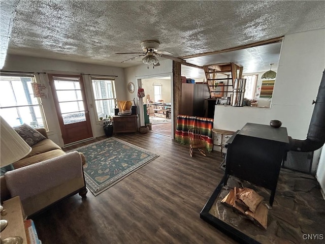 living area featuring a textured ceiling, a wood stove, a ceiling fan, and wood finished floors