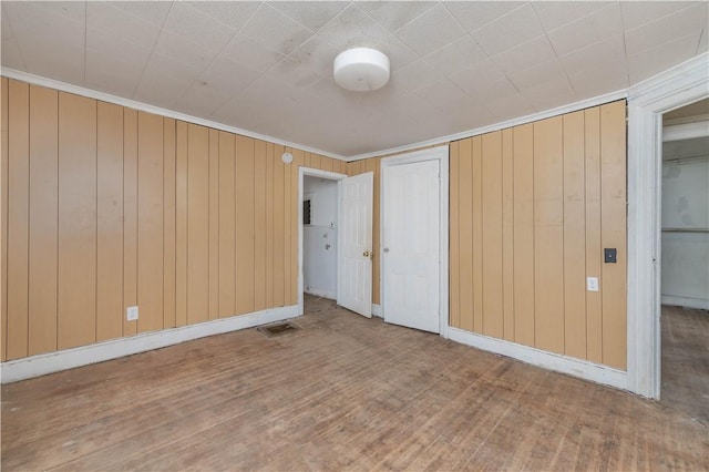 unfurnished bedroom with wooden walls, wood finished floors, visible vents, baseboards, and crown molding