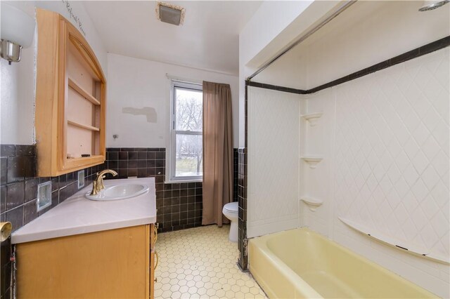 bathroom with toilet, tile walls, wainscoting, bathing tub / shower combination, and vanity