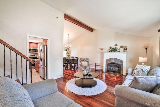 living room featuring light wood finished floors, vaulted ceiling with beams, stairs, a tiled fireplace, and a chandelier