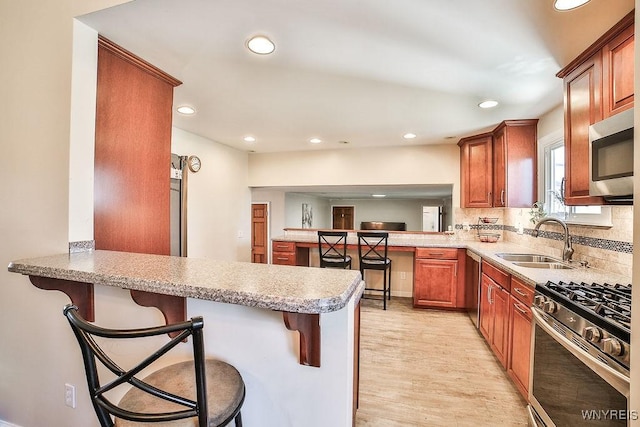 kitchen featuring light wood finished floors, tasteful backsplash, appliances with stainless steel finishes, a peninsula, and a sink