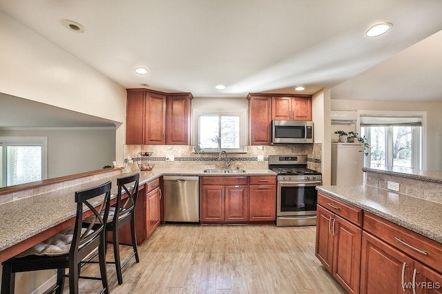 kitchen with light wood finished floors, decorative backsplash, stainless steel appliances, and a sink