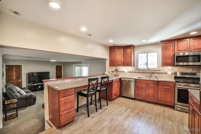 kitchen with light stone counters, a peninsula, a sink, stainless steel appliances, and backsplash