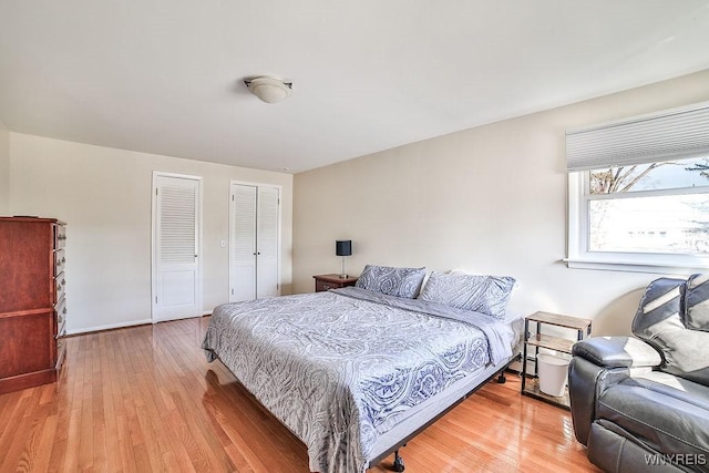 bedroom with baseboards, two closets, and light wood-style flooring