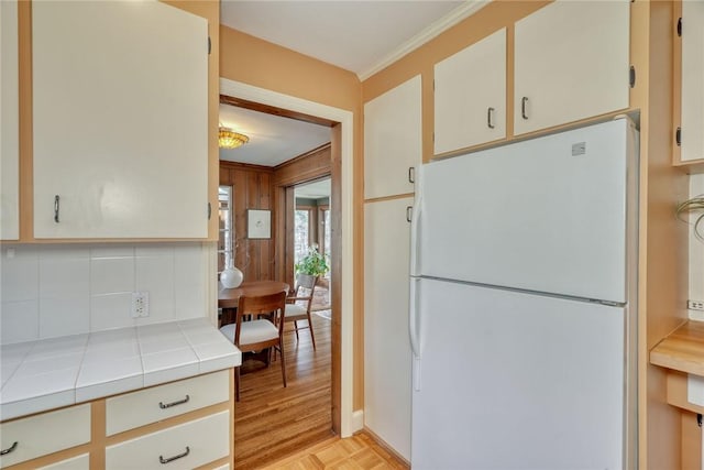 kitchen with ornamental molding, tasteful backsplash, freestanding refrigerator, tile countertops, and parquet floors