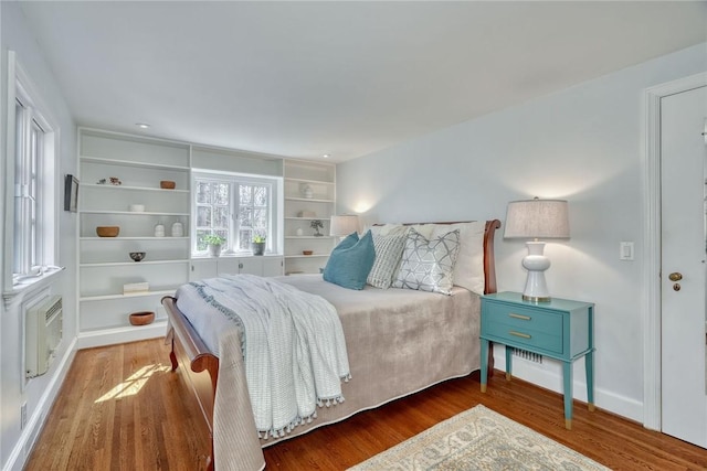 bedroom with a wall mounted air conditioner, baseboards, and wood finished floors