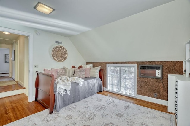 bedroom featuring a wall mounted air conditioner, visible vents, wood finished floors, lofted ceiling, and attic access