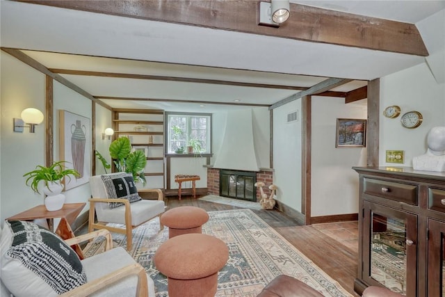 sitting room with visible vents, beam ceiling, light wood-style flooring, a fireplace, and baseboards